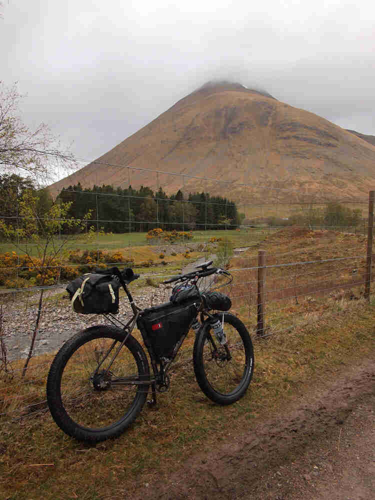 Right side view of a Surly ECR bike, loaded with gear, parked along a wire fence, with a tall hill in the background