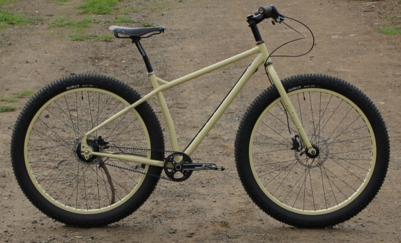 Right side view of a tan, Surly ECR bike, parked on a dirt area