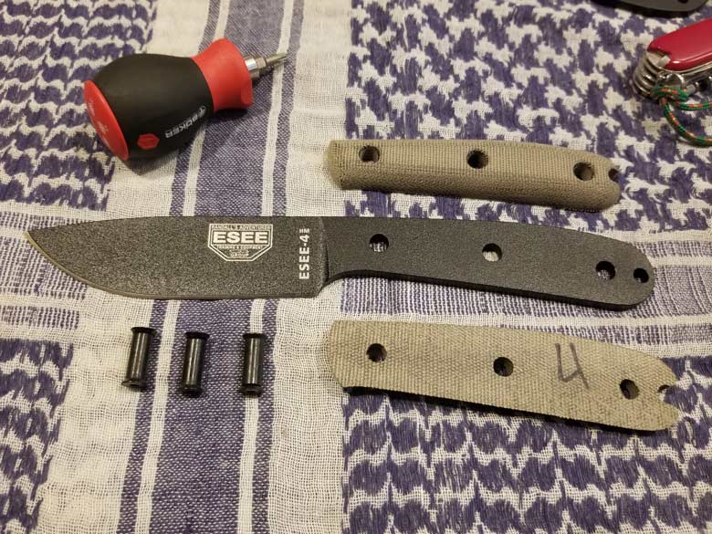 Disassembled knife with black powder coated steel and tan handles lays with black and red stubby screwdriver on blanket 