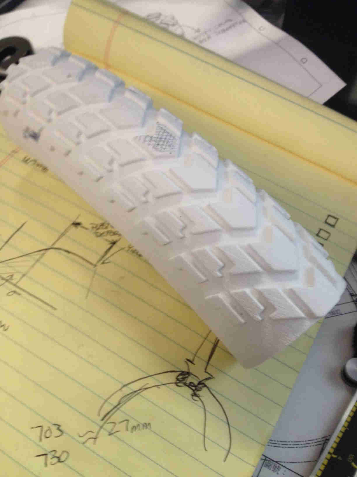 Downward view of a white bike tire cut-out, with the tread facing up, laying across a yellow legal pad - 1st