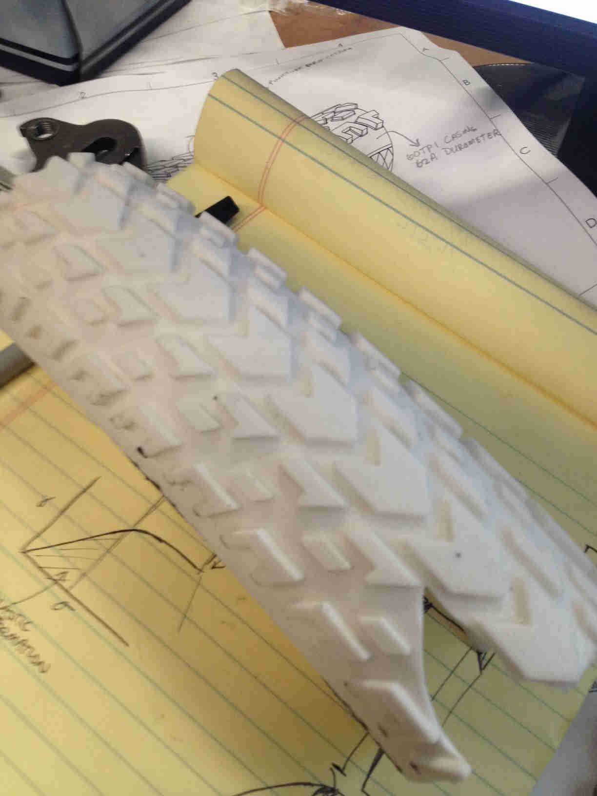Downward view of a white bike tire cut-out, with the tread facing up, laying across a yellow legal pad - 3rd