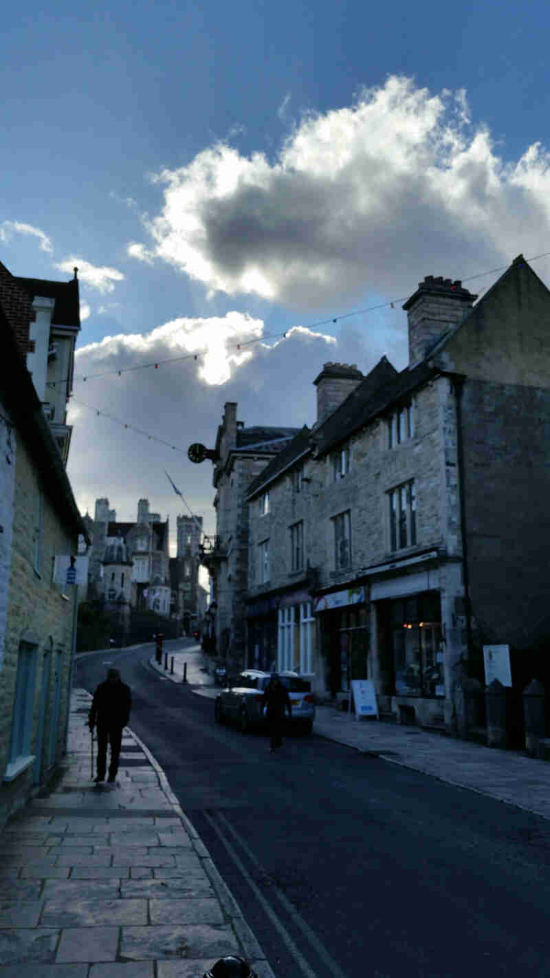 A straight view down a road with stone building on each side, with blue sky and clouds above