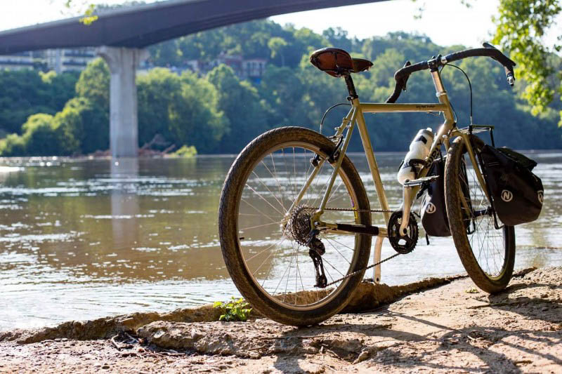 Rear right side of a Surly bike, on the bank of a river, with a bridge above in the background