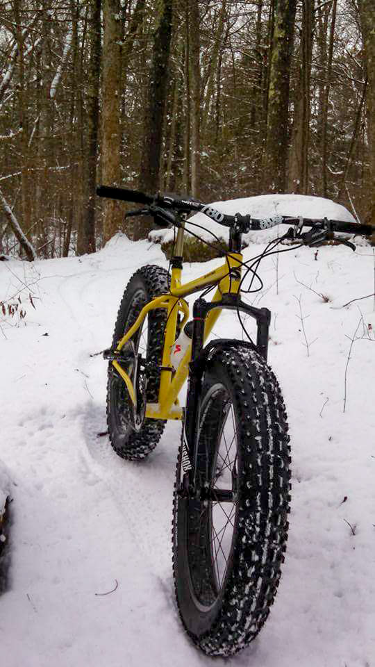 Front view of a yellow Surly fat bike, standing in the snow, with a forest in the background