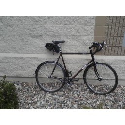 Right side view of a black Surly bike with seat pack, parked against a stone block wall on rocks