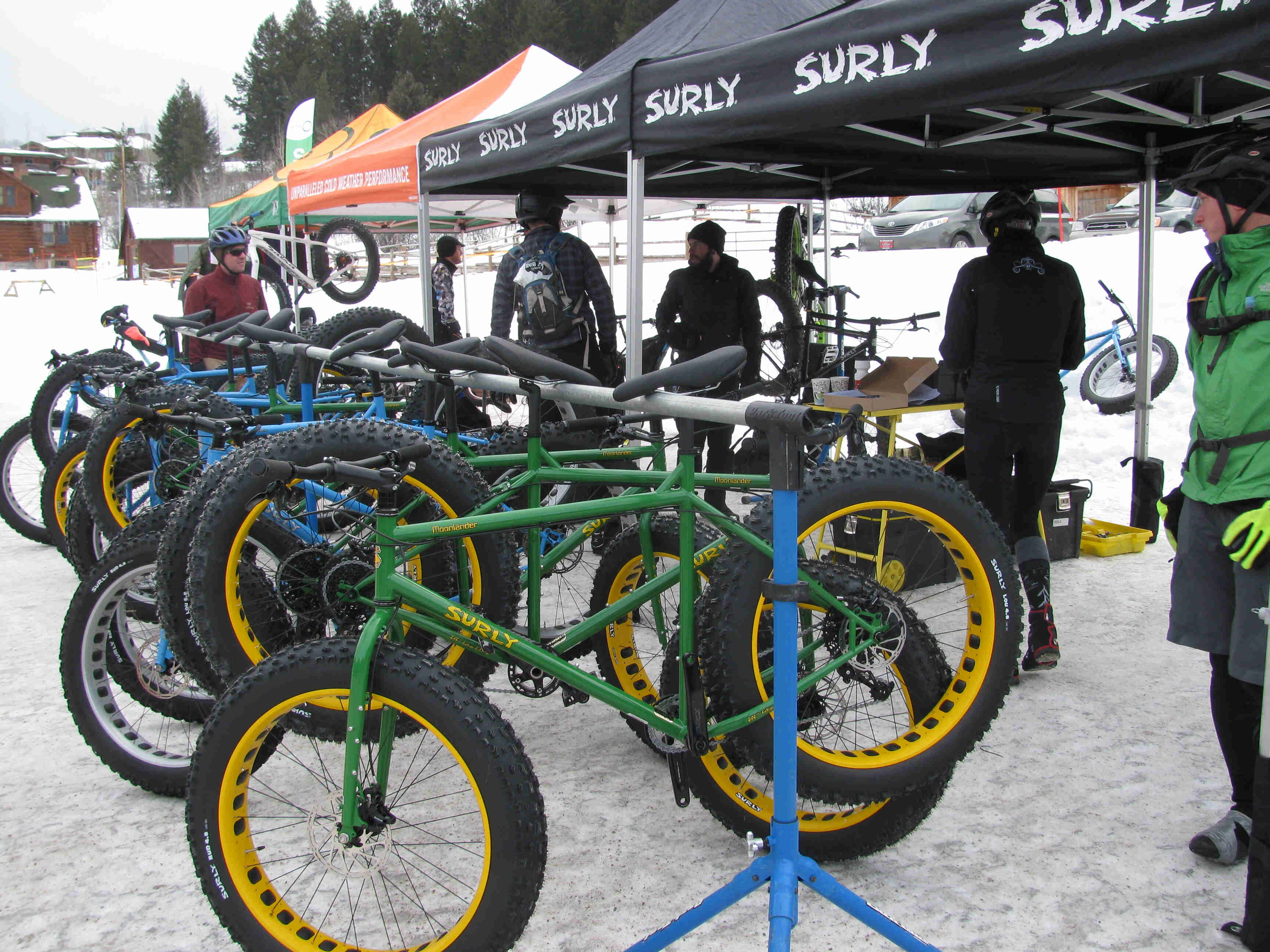 Side view of a rack, full of Surly fat bikes in the snow, with people standing behind, under a row of canopies