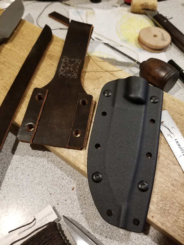 Parts of a knife sheath lay on a board with leather sewing tools
