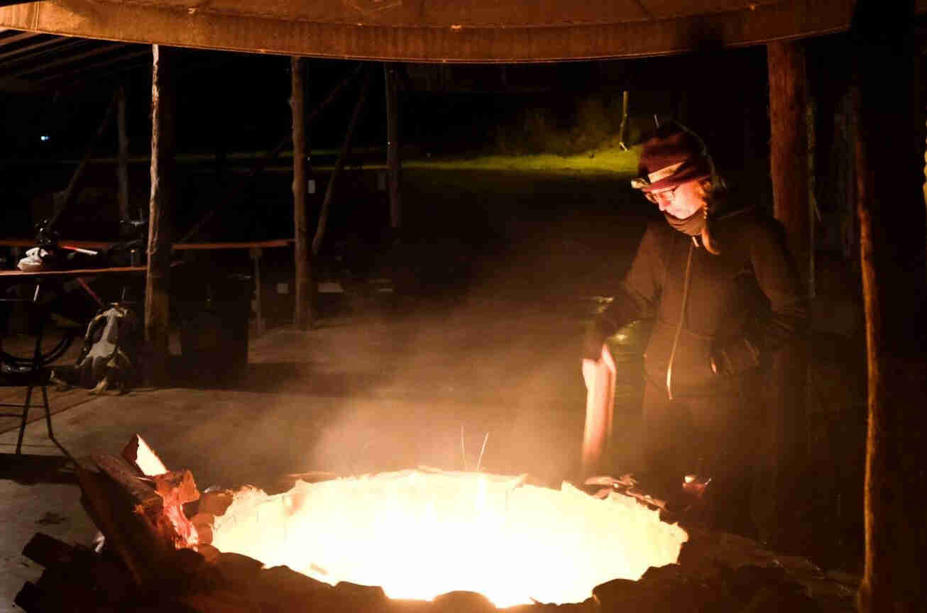 A person standing next to a campfire, under a park shelter, at night