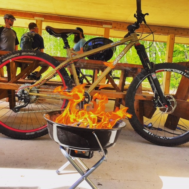 Right side view of a Surly Instigator bike, parked behind a small camp grill with fire