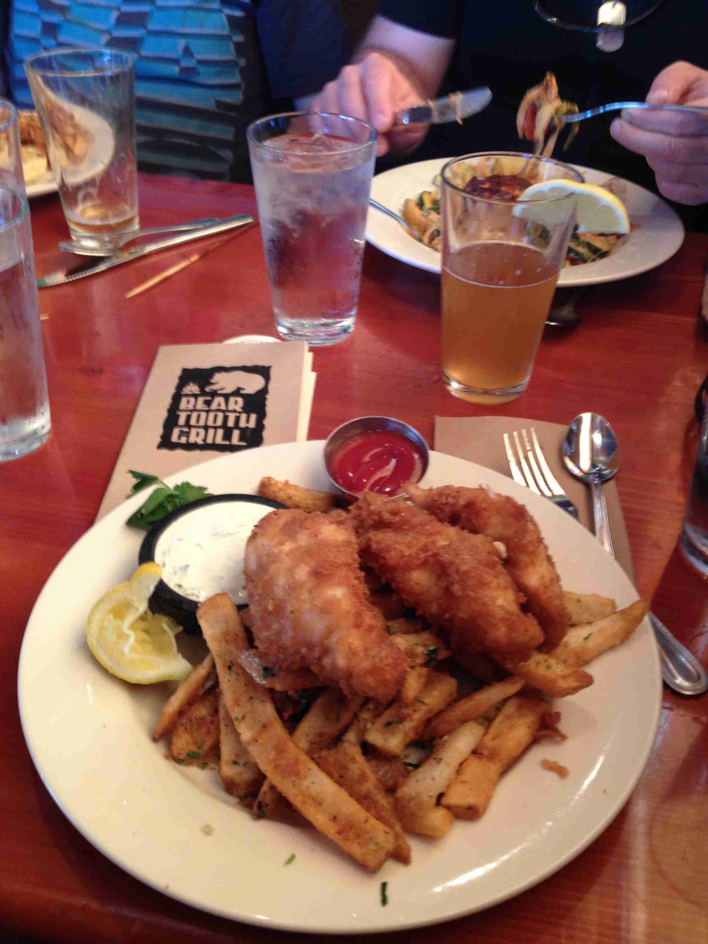 Downward view of a plate with fish and fries, sitting on a table with a glass of beer and another plate