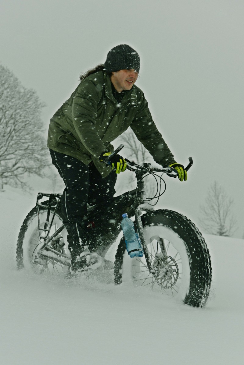 Right side view of a cyclist wearing winter outerwear, riding a Surly fat bike through deep snow