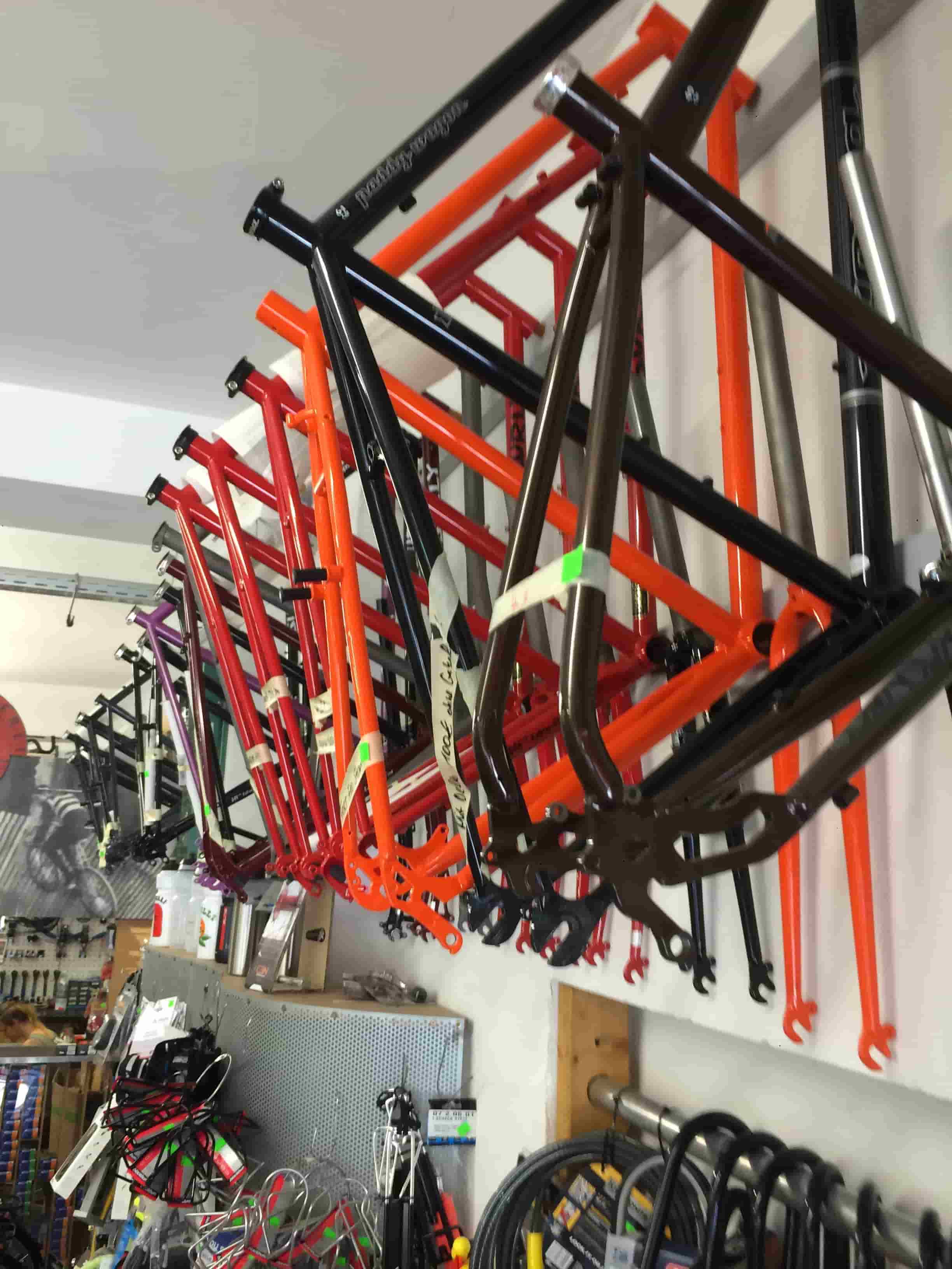 Side view of a row of Surly bike frames, hanging from a rack on a wall, near the ceiling of a bike shop