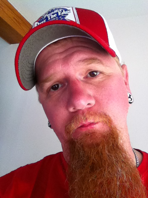 Headshot of a person wearing a hat, with a long, narrow beard and sunburned face