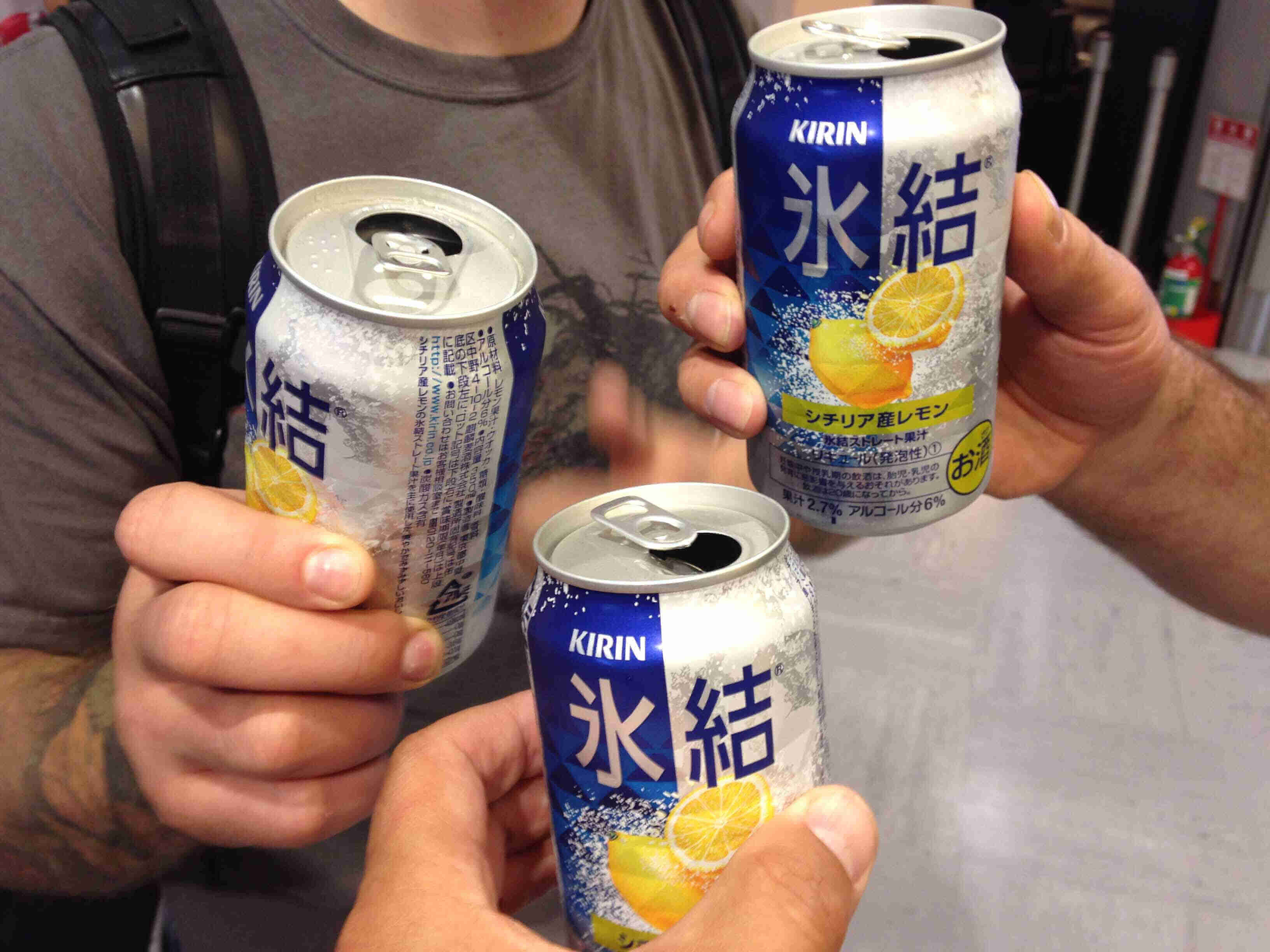 Three hands holding up 3 beverage cans with lemons and Japanese text on them