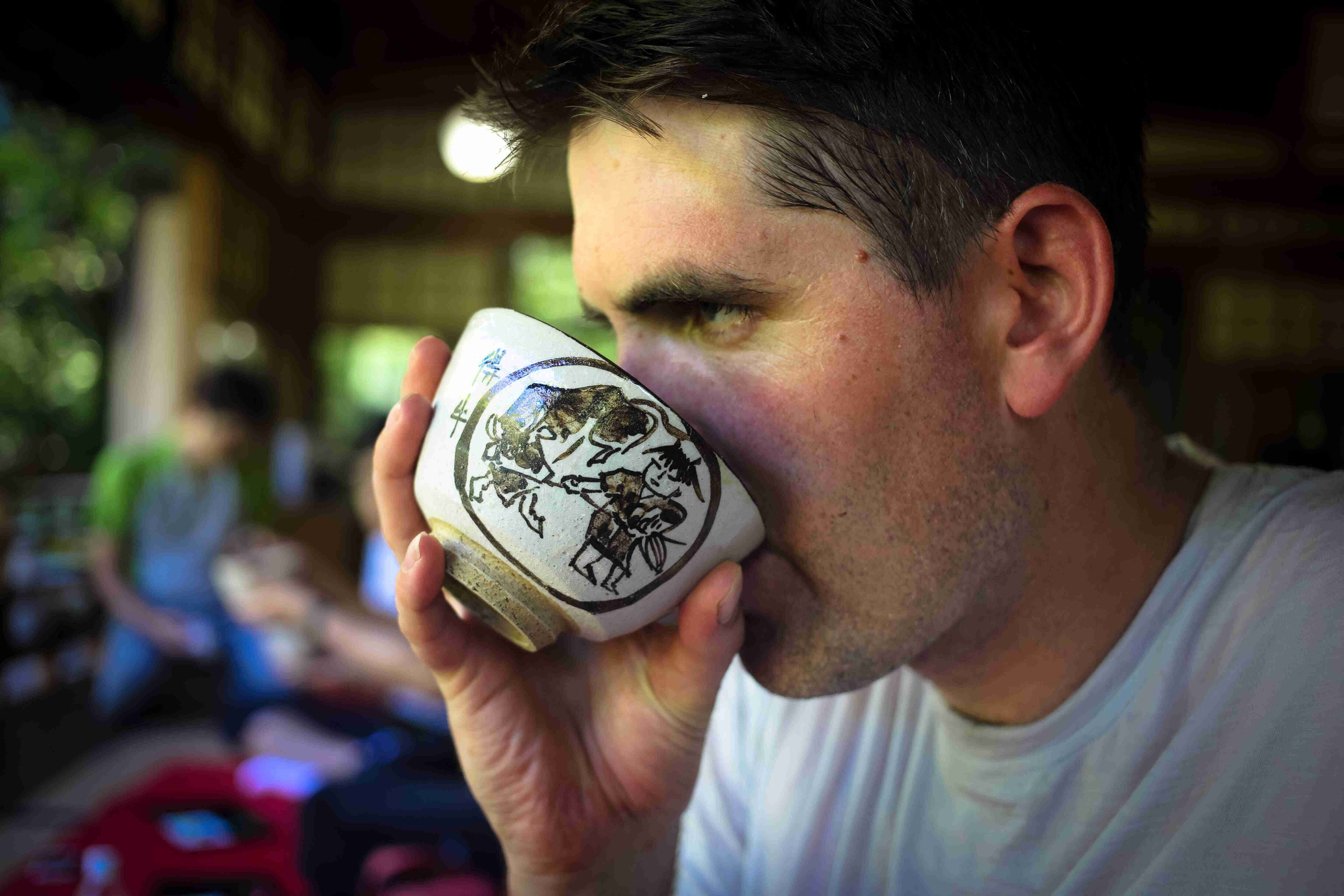Right side head shot of a person drinking tea from a bowl with a Japanese painting on it