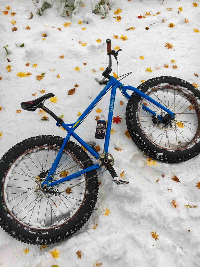 Right side view of a blue Surly fat bike, laying in the snow, on it's left side