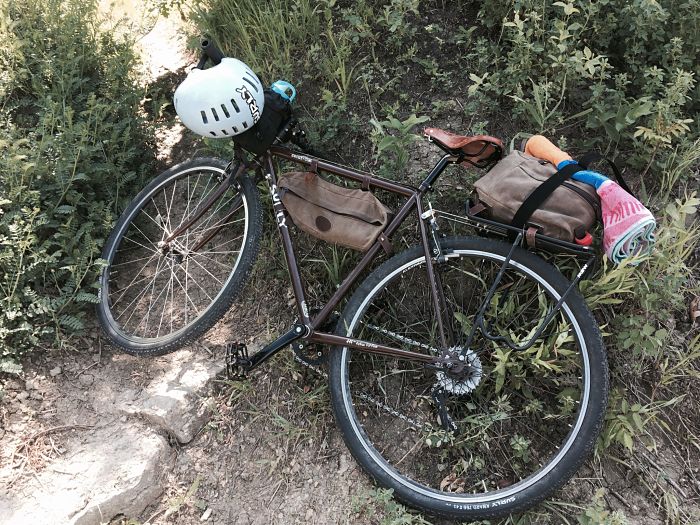 Downward view of a Surly Cross Check bike, brown, laying on it's right side, in the weeds