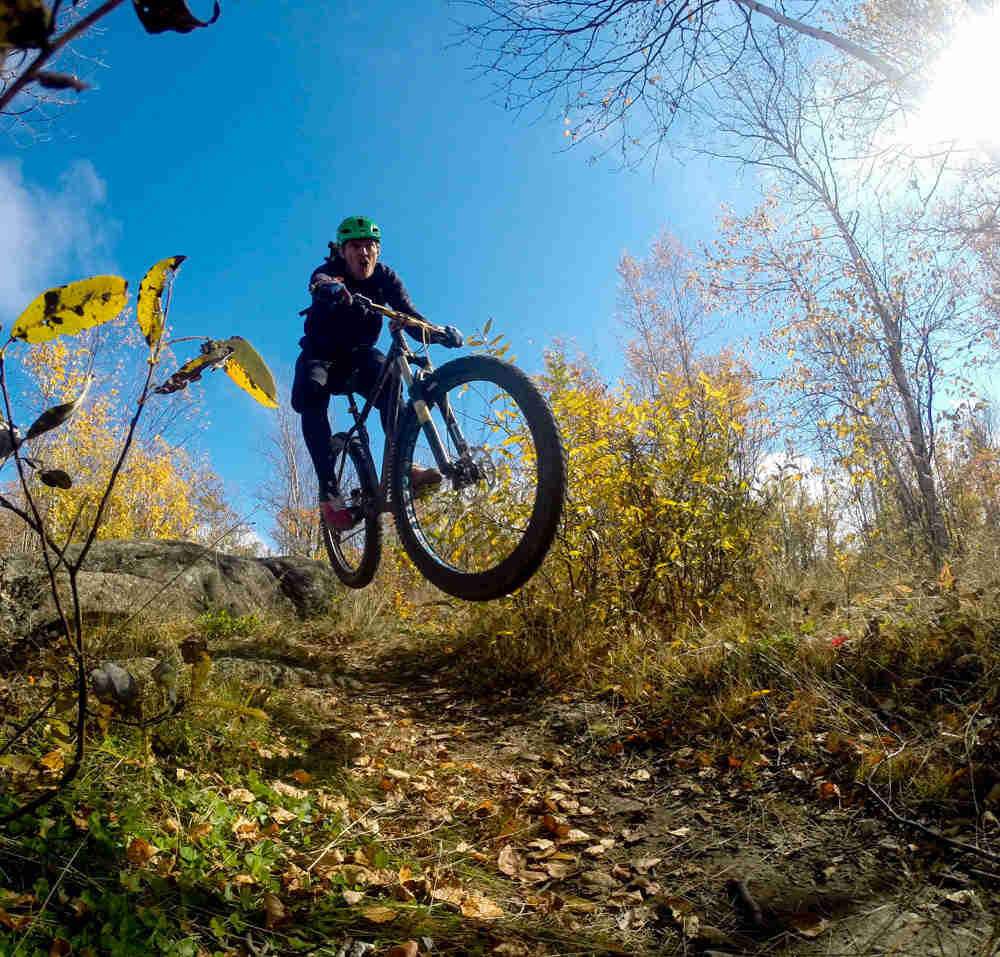 Front view of a cyclist riding a Surly Krampus Ops bike, jumping off a rock on a dirt trail in the woods