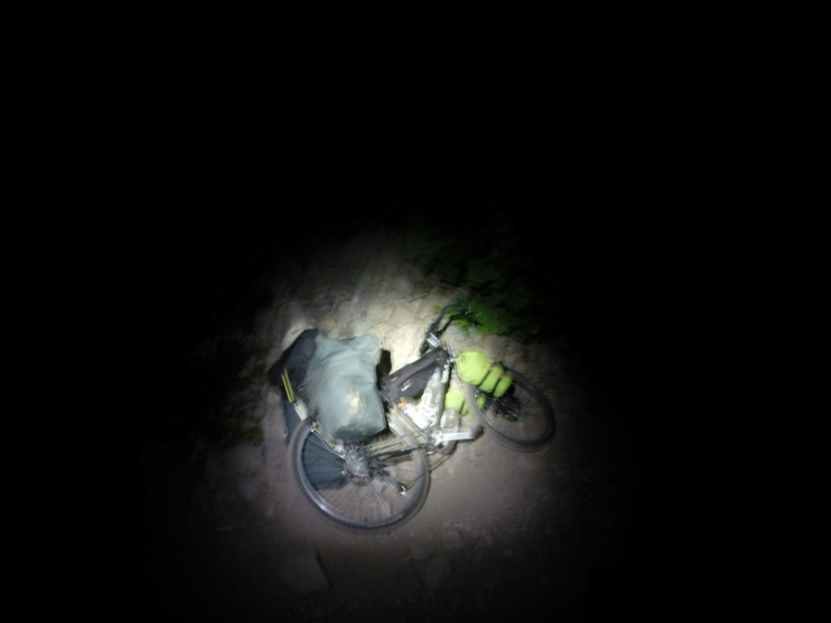 Blurred, downward, right side view of a bike, loaded with gear, laying on it's side, on dirt at night