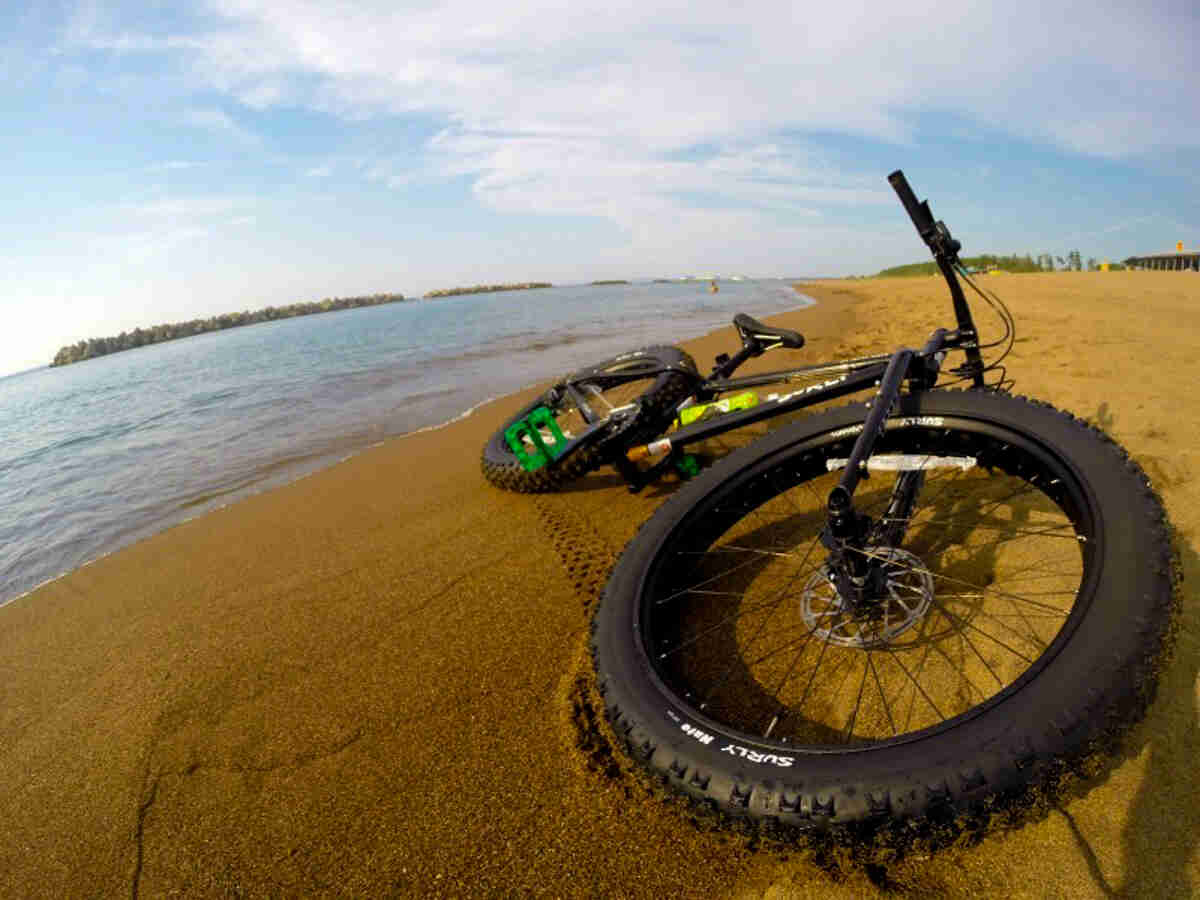 Front, ground level view of a black Surly fat bike, laying on it's left side, on a sandy beach