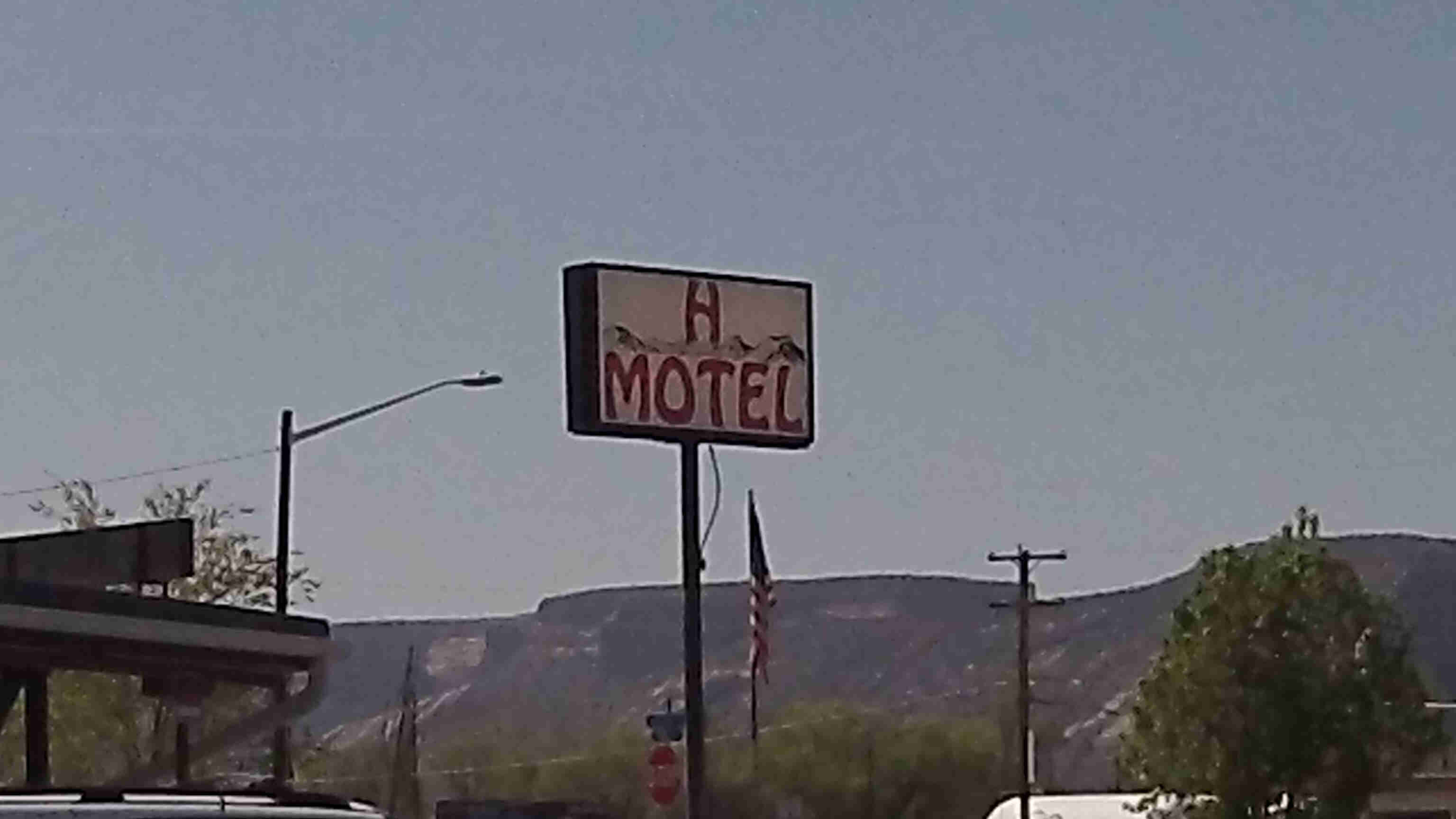 Front view of a sign for the H Motel, with desert buttes in the background