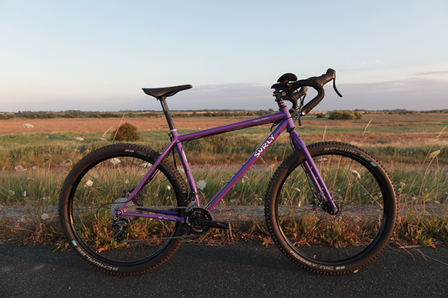 Right view of a Surly road bike, purple, with grassy plains and hazy sky in the background