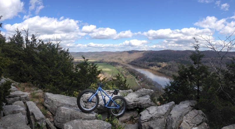Left side view of a blue Surly Ice Cream Truck bike, parked on large rocks, with a river and mountains in the background