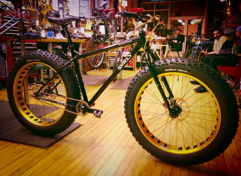 Right side view of a Surly Ice Cream Truck fat bike, black, parked on the wood floor of a bike shop