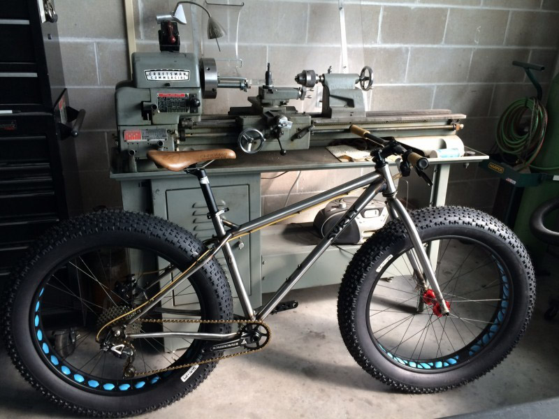 Right side view of an unpainted Surly Ice Cream Truck fat bike, parked alongside a tooling machine in a workshop