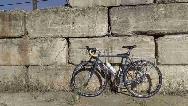 Left side view of a light blue Surly bike, parked against a large block, stone wall