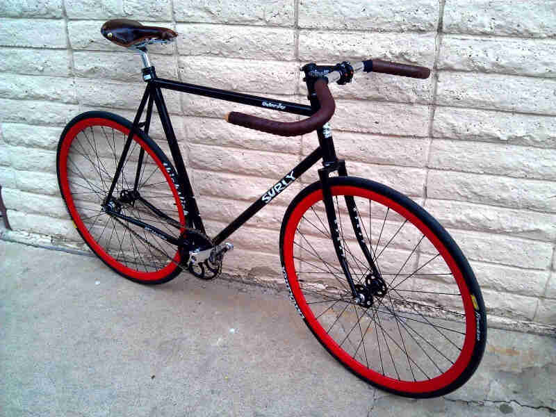 Right side view of a view of a black Surly Steamroller bike with red rims, leaning against a white, stone block wall