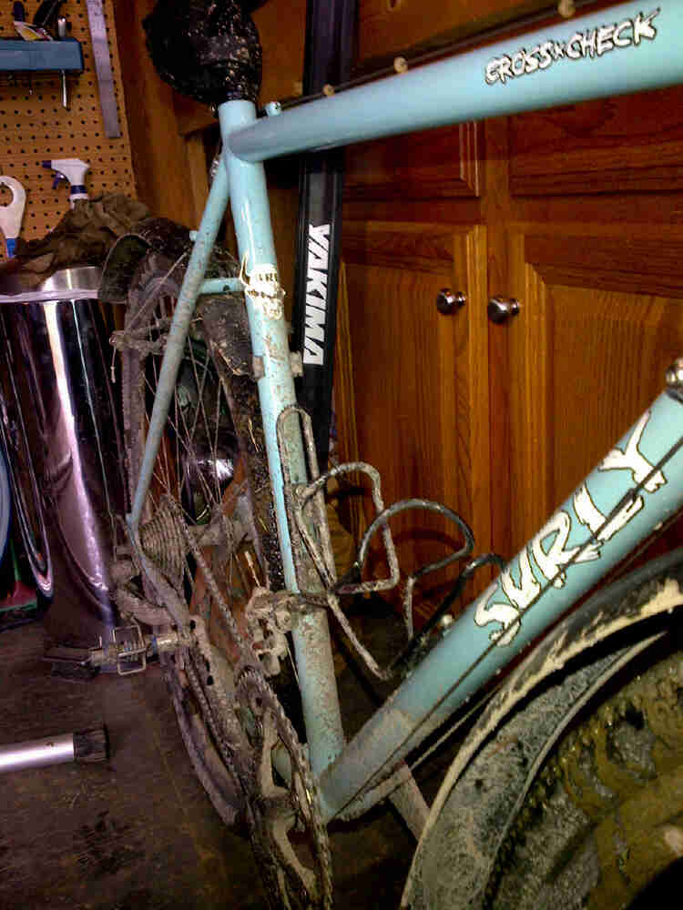 Cropped, right side angled view of a dirty, light blue Surly Cross Check bike in a garage