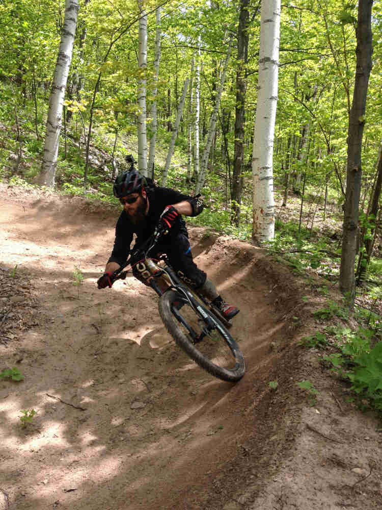 Front view of a cyclist riding a Surly Instigator bike, rounding a small berm, on a dirt track in the forest