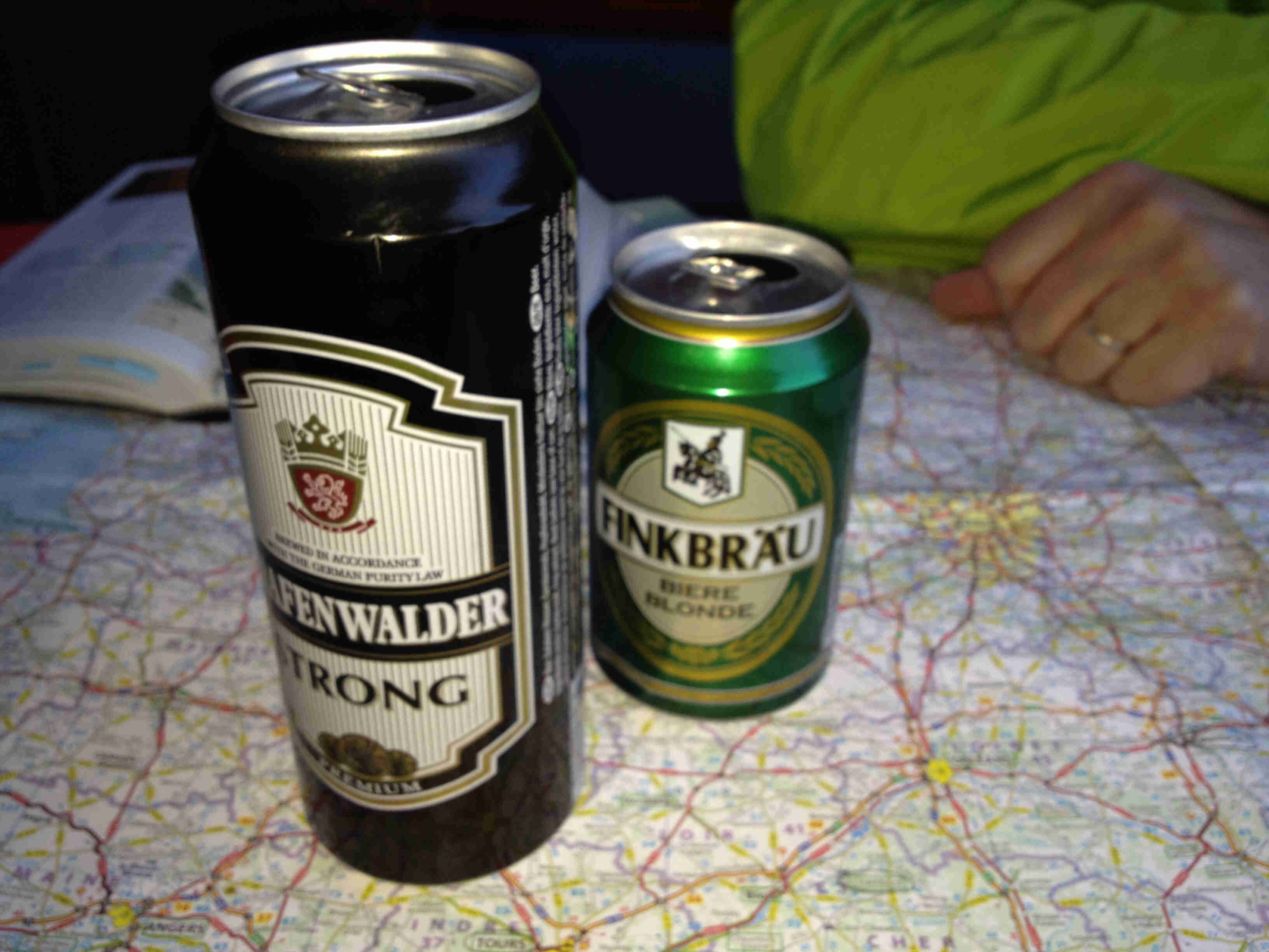 Side view of 2 beer cans, standing on top of a paper map