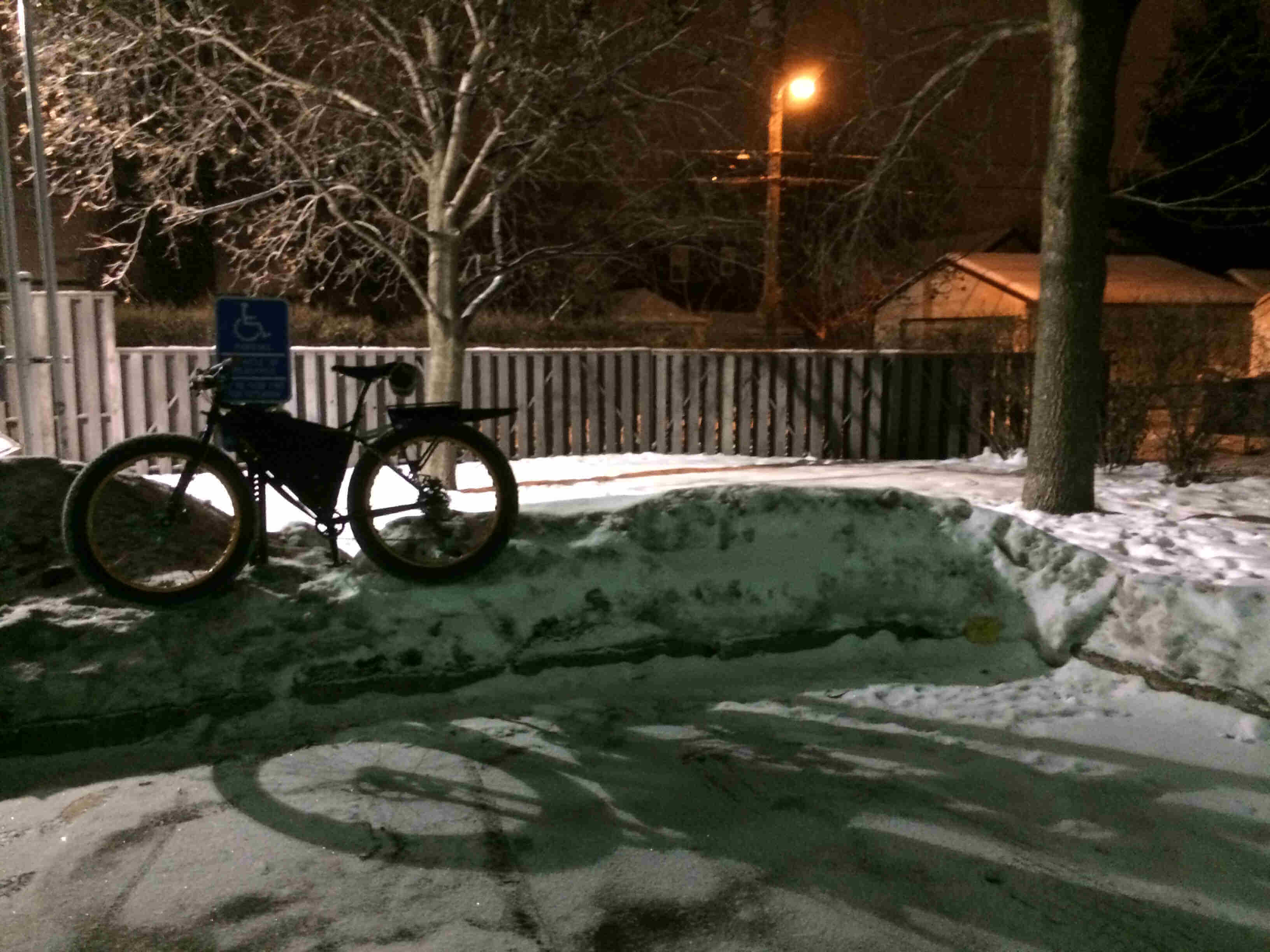 Left side view of a Surly Pugsley fat bike, standing on a snowbank, against a handicap parking sign at night