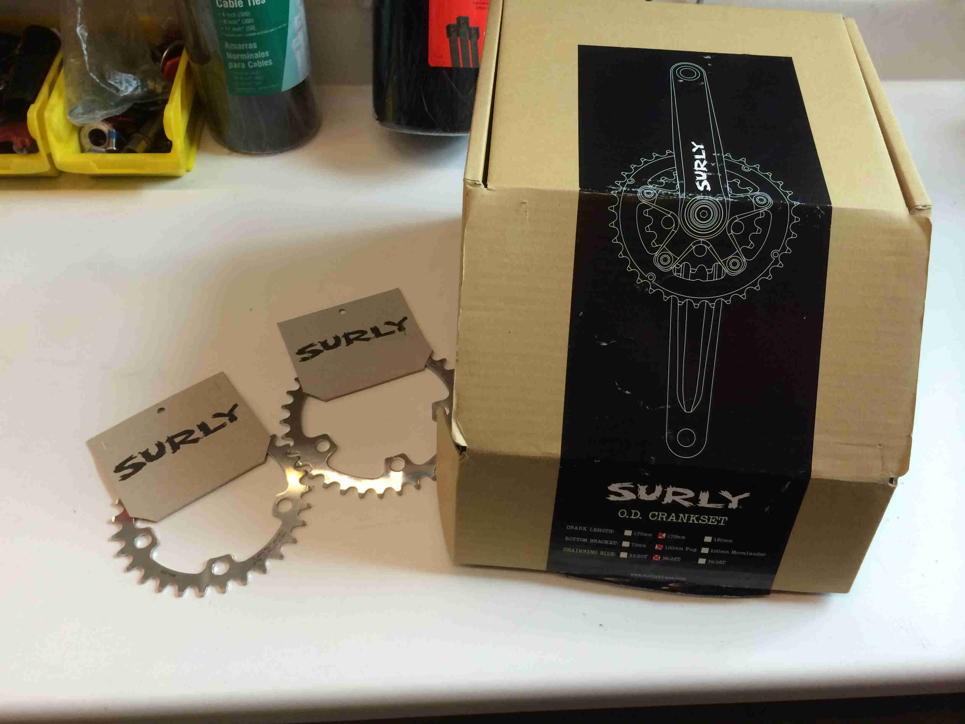 Two Surly Bikes chainrings, sitting on a table next to a  box with a label that shows a graphic of a Surly O.D Crankset