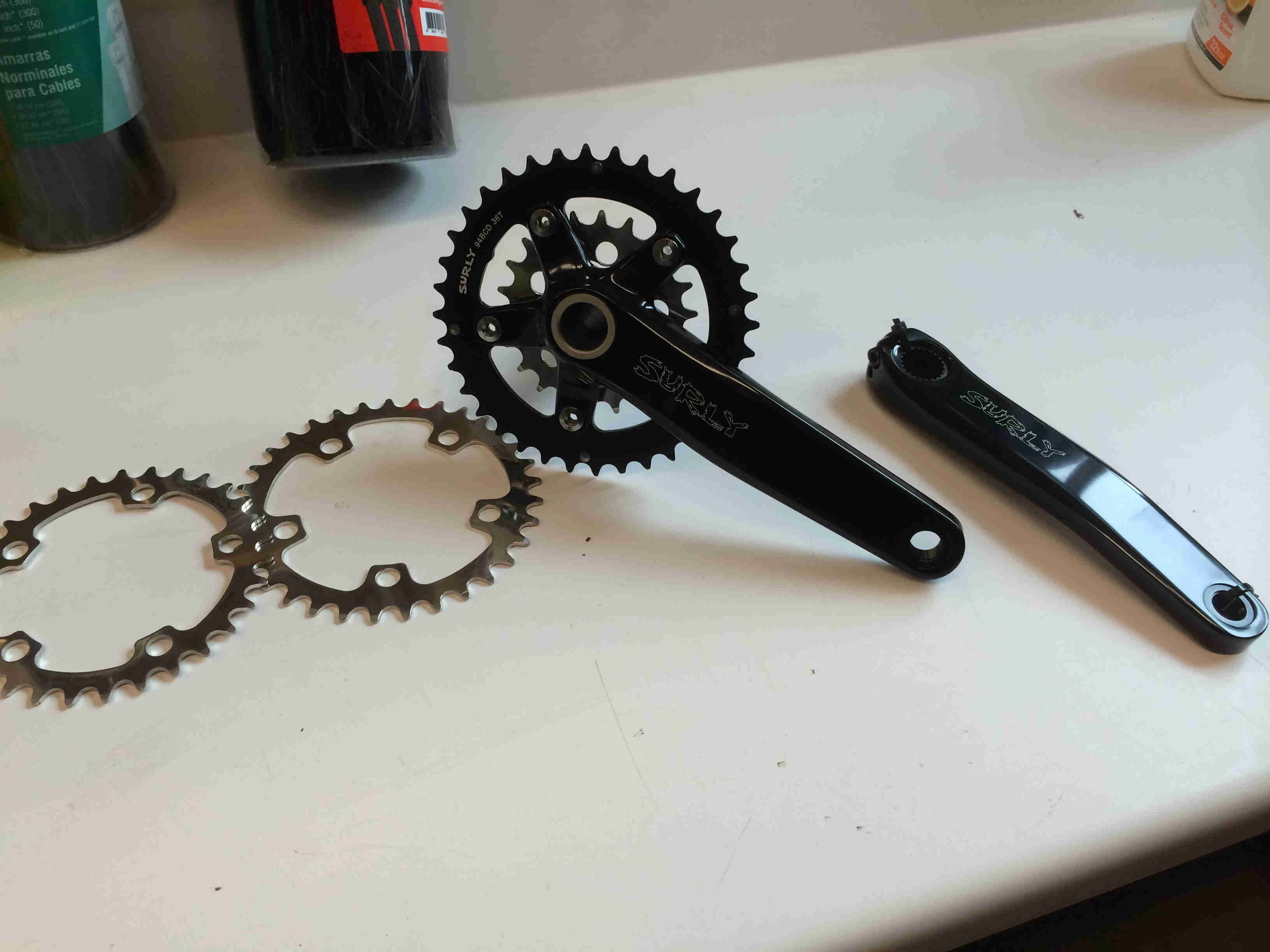 Two chainrings, sitting on a table, next to a Surly Bikes O.D Crankset
