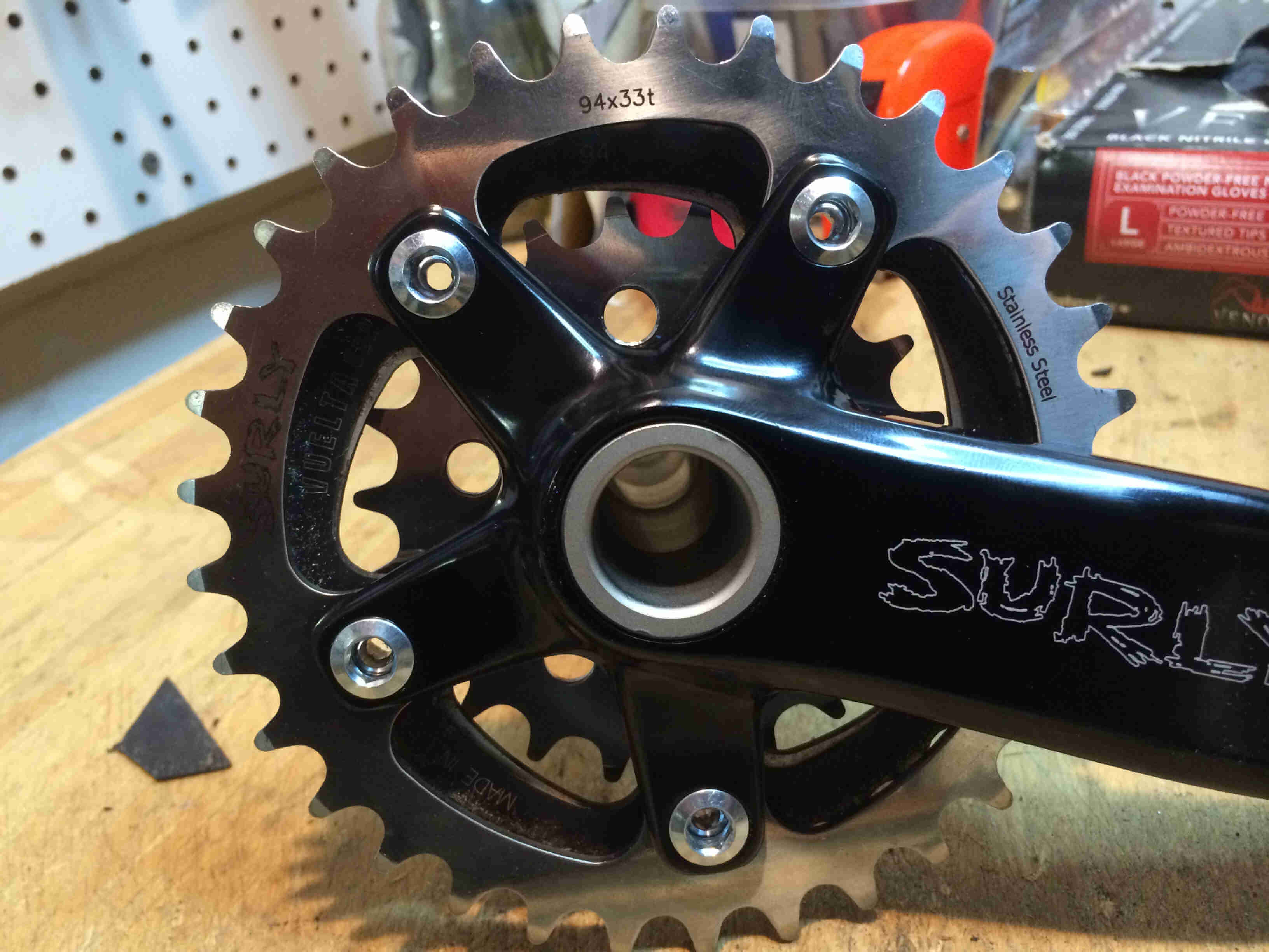Side view of a Surly Bikes O.D Crankset, outer drivetrain side detail, sitting on a wood workbench