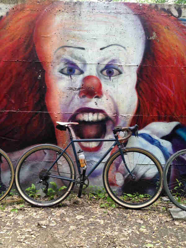 Right side view of a bike parked against a wall with a mural of Pennywise the clown