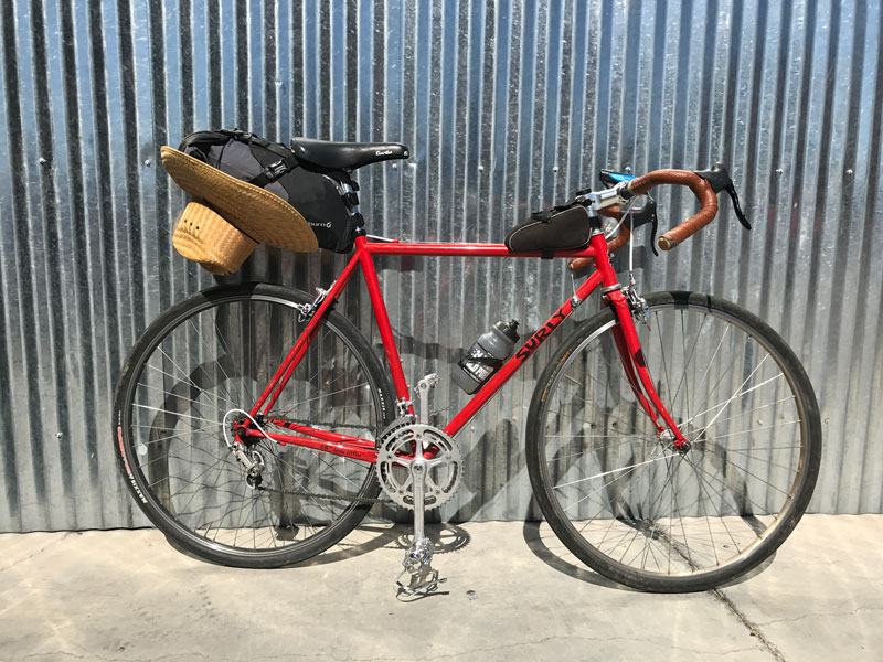Right side view of a Surly bike, red, parked against a corrugated steel wall