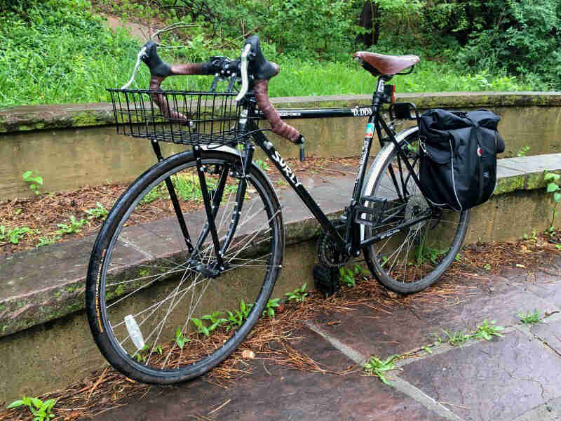 Left side view of a black Surly Cross Check bike with a rear pack, parked along a short stone wall alongside a canal