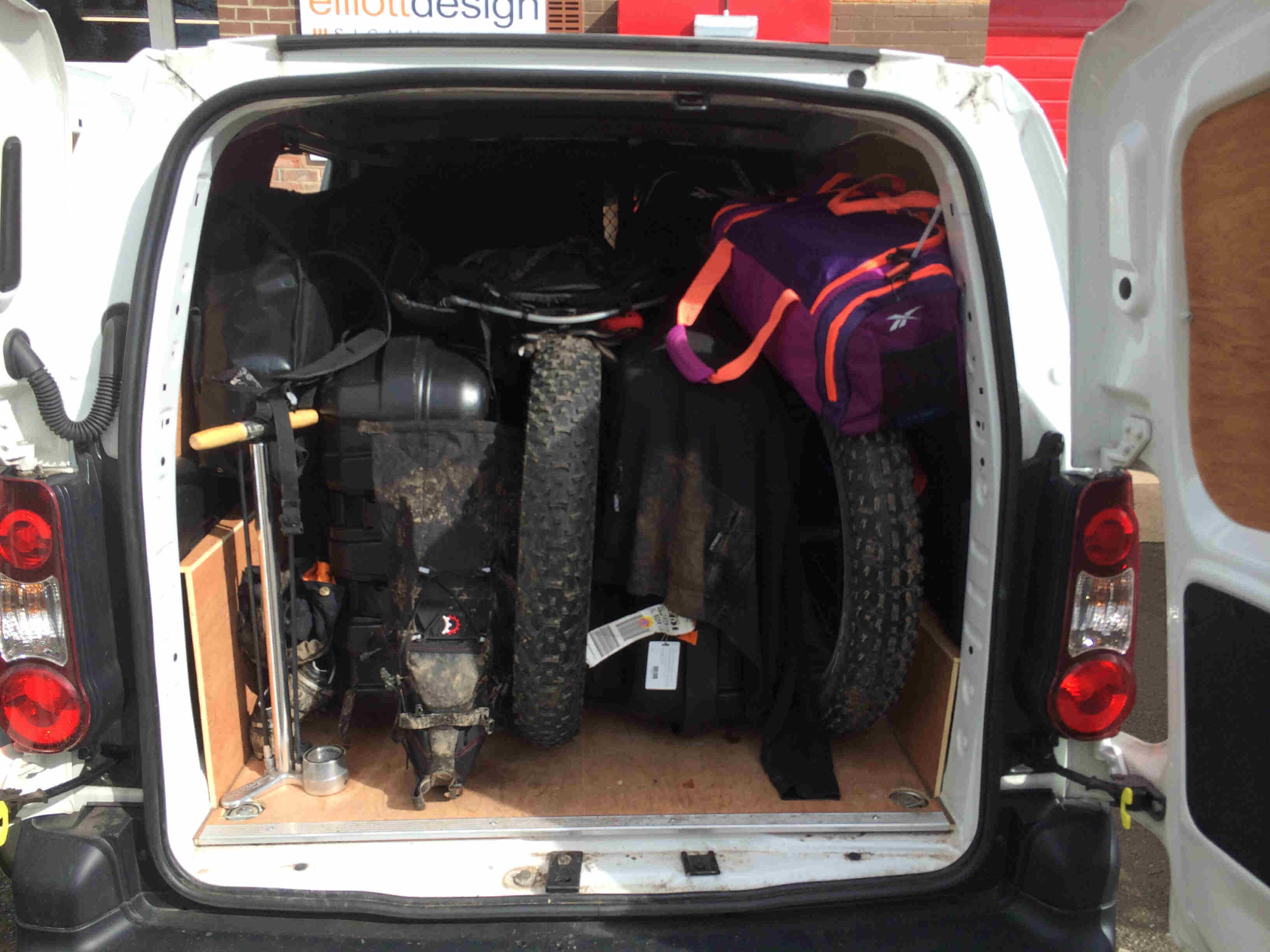 Rear view into a van with open back doors, loaded with fat bikes and gear
