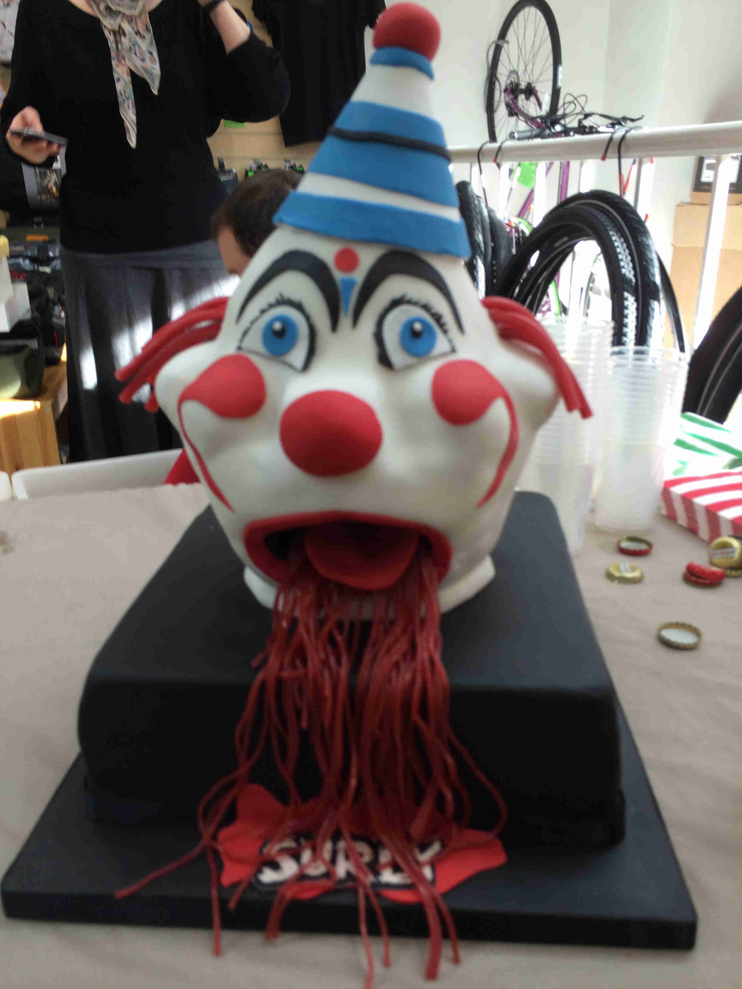 Front, close up of a clown head mask, mounted on top of a black base with a Surly patch on it, sitting on  a table