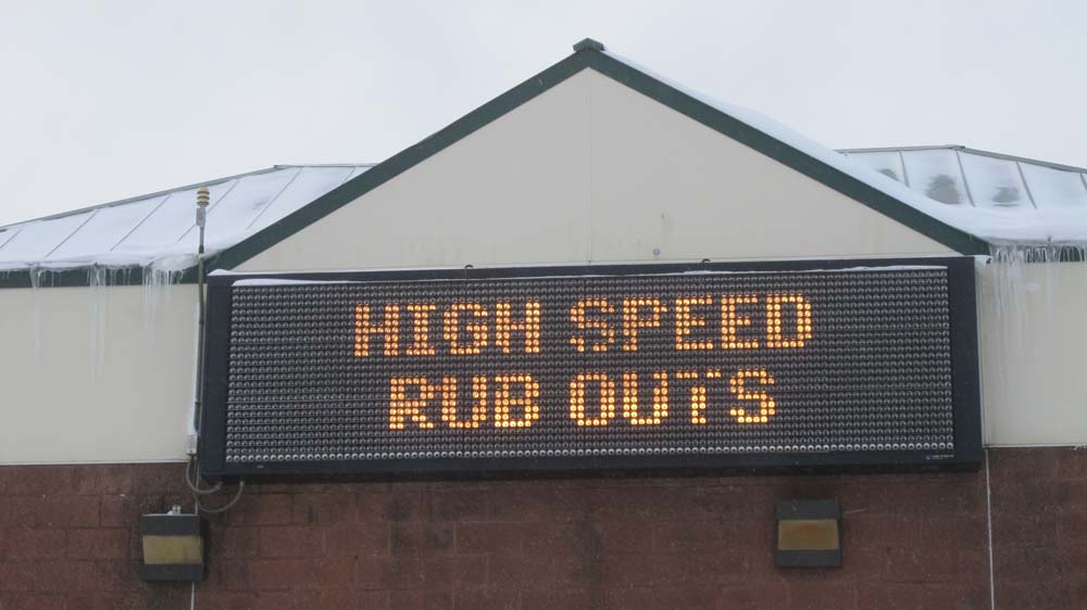 Front view of a digital sign on a building that shows, HIGH SPEED RUB OUTS, on it