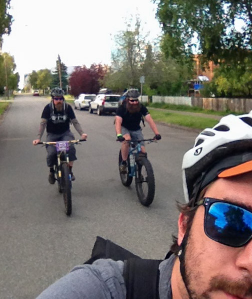 Close up, front view of half a person's face on the right, with two cyclists riding Surly bikes on the street, behind