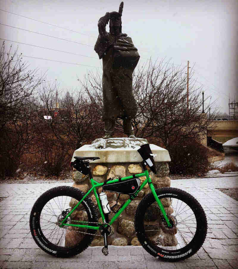 Right side profile of a green Surly bike in front of a Native American monument 