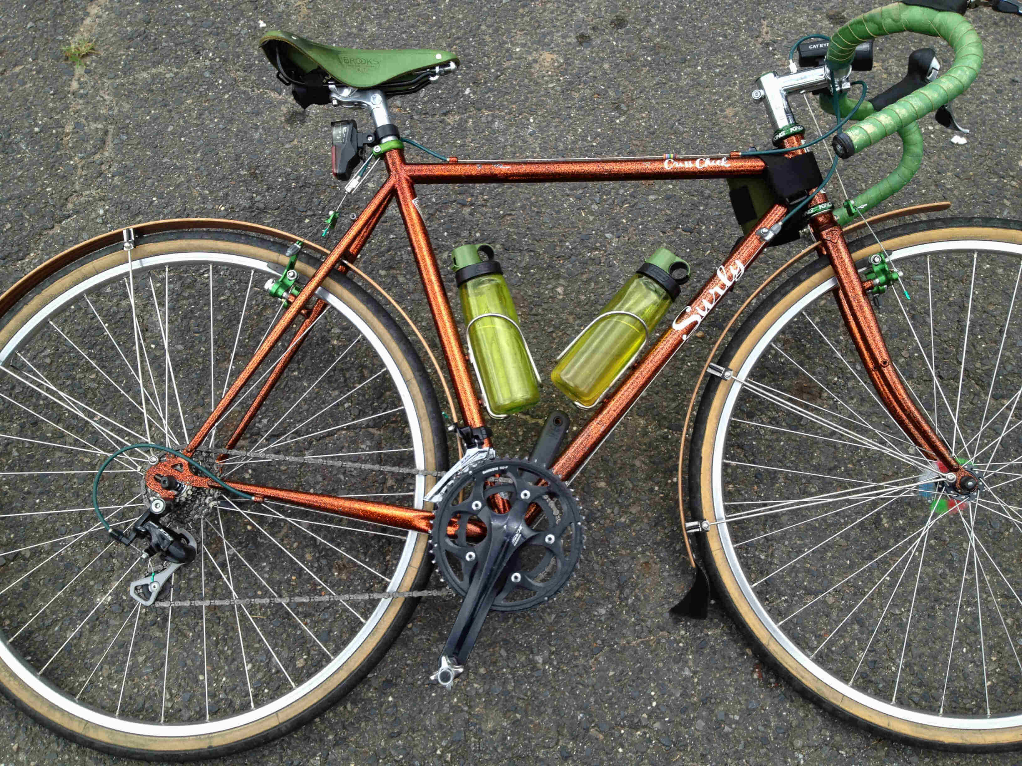 Downward, right side view of a copper Surly Cross Check bike, laying on it's left side on pavement