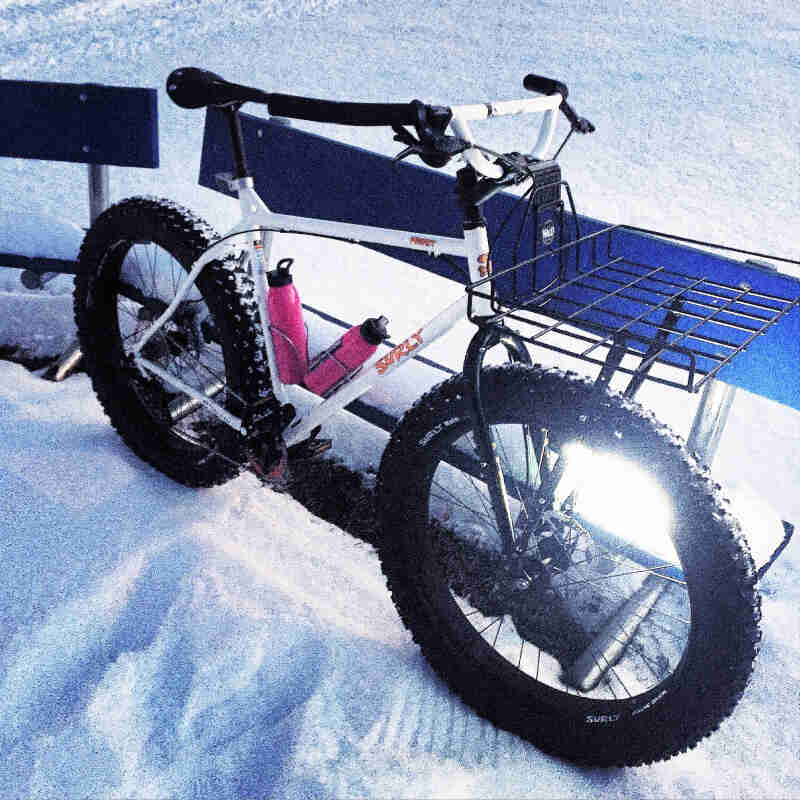 Right side view of a white Surly Pugsley fat bike, parked in the snow against a bench