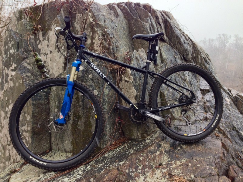 Left side view of a black Surly Troll bike, leaning against a mountain peak