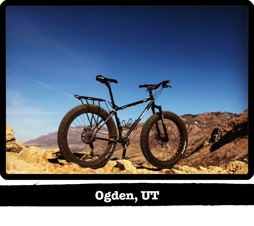 Right side view of a black Surly fat bike on rocks with mountain hills behind-Ogden, UT banner below image